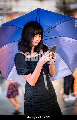 A beautiful Filipino girl keeps dry from the rain under an umbrella in Manila, The Philippines. Stock Photo