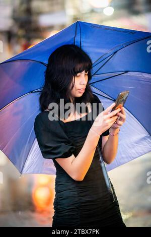 A beautiful Filipino girl keeps dry from the rain under an umbrella in Manila, The Philippines. Stock Photo