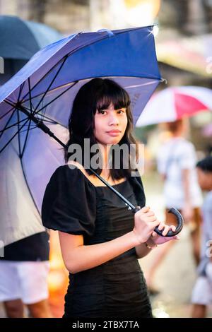 A beautiful Filipino girl keeps dry from the rain under an umbrella in Manila, The Philippines. Stock Photo