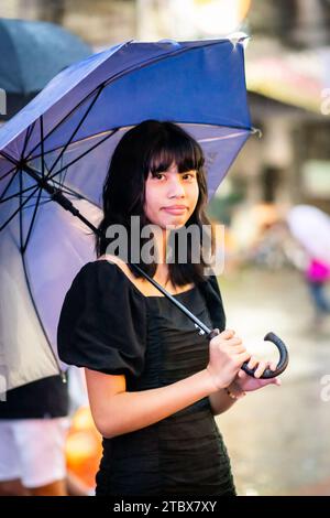 A beautiful Filipino girl keeps dry from the rain under an umbrella in Manila, The Philippines. Stock Photo