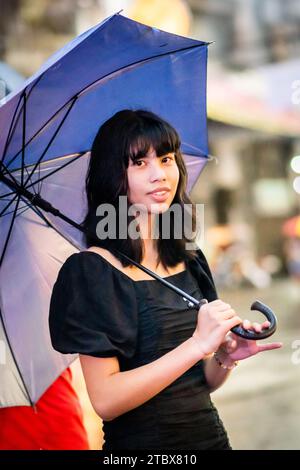 A beautiful Filipino girl keeps dry from the rain under an umbrella in Manila, The Philippines. Stock Photo