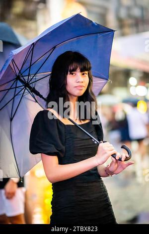 A beautiful Filipino girl keeps dry from the rain under an umbrella in Manila, The Philippines. Stock Photo