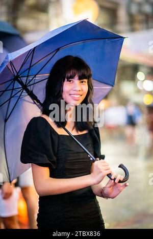 A beautiful Filipino girl keeps dry from the rain under an umbrella in Manila, The Philippines. Stock Photo