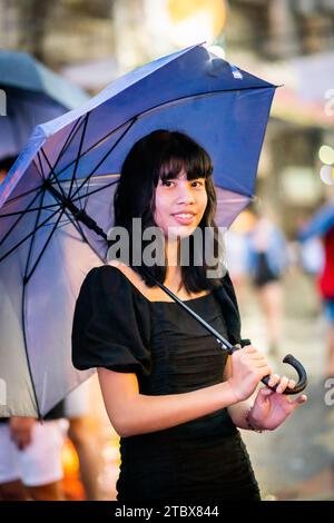 A beautiful Filipino girl keeps dry from the rain under an umbrella in Manila, The Philippines. Stock Photo