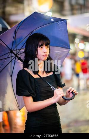 A beautiful Filipino girl keeps dry from the rain under an umbrella in Manila, The Philippines. Stock Photo