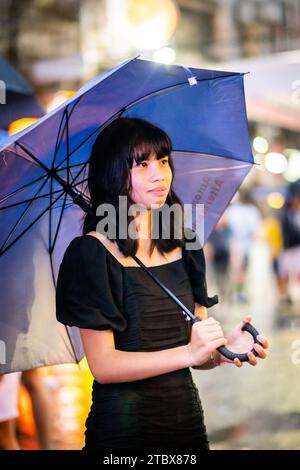 A beautiful Filipino girl keeps dry from the rain under an umbrella in Manila, The Philippines. Stock Photo