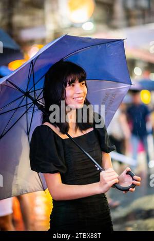 A beautiful Filipino girl keeps dry from the rain under an umbrella in Manila, The Philippines. Stock Photo