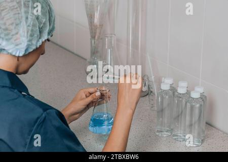 woman in protective cap in laboratory checks water quality using glass tube filled with blue chemical liquid for research and analysis in laboratory Stock Photo