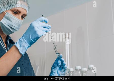 Woman in mask and rubber gloves in laboratory examines quality of water with glass tube filled with blue chemical liquid for research and analysis in Stock Photo