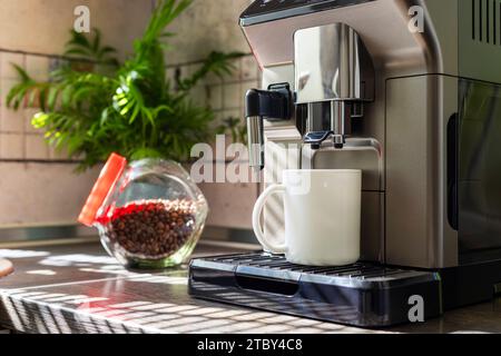 Modern electric coffee machine with cup on countertop in kitchen Stock Photo