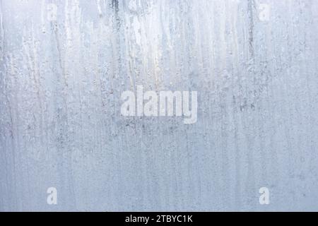 Winter window with frozen vertical water stripes. Melting frosty patterns on winter frozen white window glass. Magic of nature. Christmas or winter ho Stock Photo