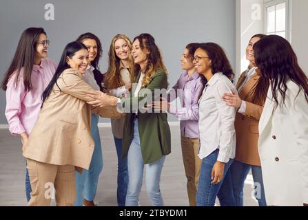 Happy cheerfull young diverse women friends or coworkers hugging and laughing on grey background. Stock Photo