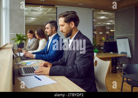 Business people sitting in a row and working on laptop computers in modern open plan office. Stock Photo