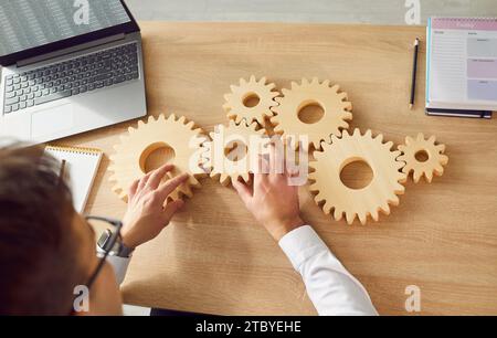 Top view of business man connecting big wooden gears together sitting at the desk on his workplace Stock Photo