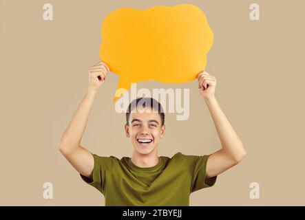 Happy young boy holding blank speech bubble for thoughts on studio beige background. Stock Photo