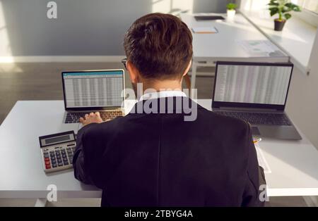Financial accountant sitting at his office desk and working with data sheets on laptops Stock Photo