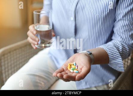 woman holding a glass of water and taking vitamins and pills on a light background. close up. Stock Photo