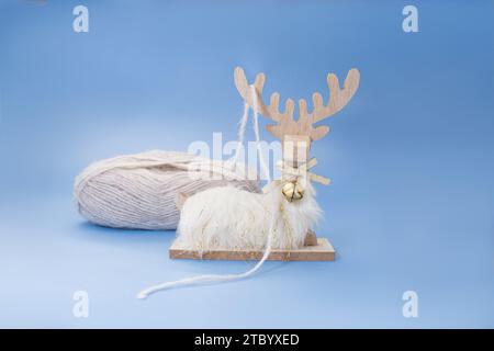 Yarn of gray wool in slide and wooden white fluffy deer on blue background. Concept of sewing, knitting, handmade. Copy space Stock Photo