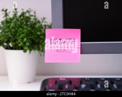 A pink paper notes with the reminder Update on it sticked on to a monitor at an office workplace. Stock Photo
