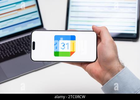 Google Calendar logo on the screen of a smartphone in mans hand with laptop and tablet with graphical diagrams on the background, December 2023, Prague, Czech Republic. Stock Photo