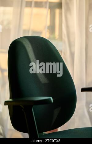 Empty black office chair with armrest with sunlight falling across the back Stock Photo