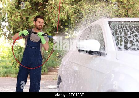 Worker washing auto with high pressure water jet at outdoor car wash Stock Photo