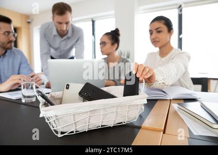 Female employee put smartphone in box at meeting Stock Photo