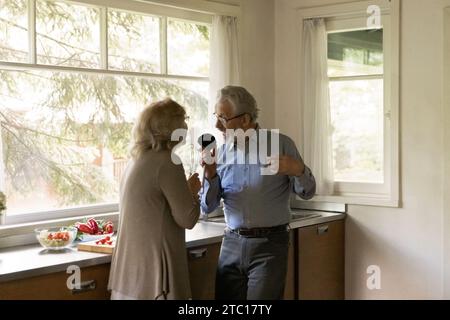 Older spouses sing at kitchen creating funny karaoke preparing food Stock Photo