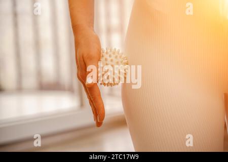 Athletic slim caucasian woman doing thigh self-massage with a massage ball indoors. Self-isolating massage Stock Photo