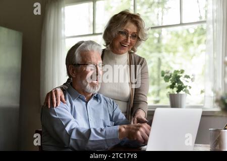 Amazed elderly married couple hug point fingers on pc screen Stock Photo