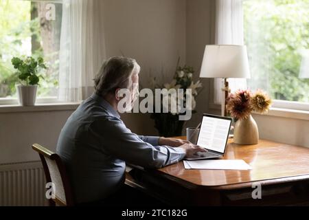 Mature aged man writer typing on laptop working on book Stock Photo