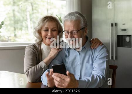 Curious aged wife watch husband playing game on mobile phone Stock Photo