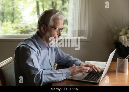 Senior man retiree wearing glasses working browsing news on laptop Stock Photo