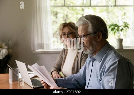 Smiling aged wife watching surprised senior husband reading paper letter Stock Photo