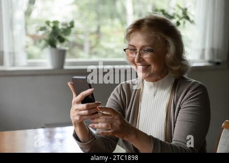 Happy female pensioner holding mobile phone enjoy using web app Stock Photo
