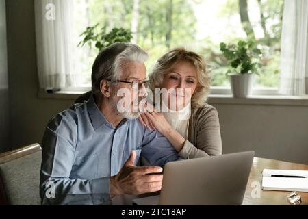 Happy elderly couple look on laptop screen feel pleasantly surprised Stock Photo