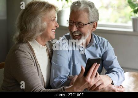Joyful older spouses embrace relax with cell discuss funny video Stock Photo