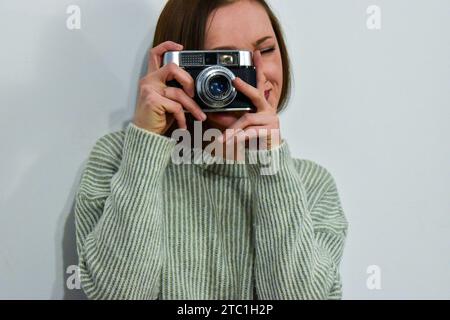 A portrait of a Caucasian young woman smiling and holding a vintage film camera in her hands Stock Photo