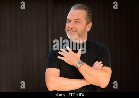 Attractive gray-haired man wearing a black T-shirt and showing his stylish watch, in front of a wooden wall Stock Photo