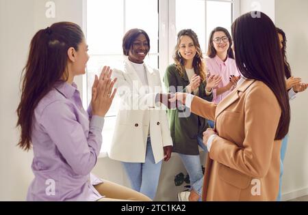 Two businesswomen shaking hands while colleagues applauding them in office Stock Photo