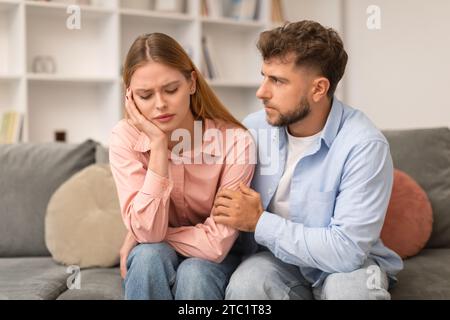 Husband Comforting Supporting Depressed Wife Sitting On Couch At Home Stock Photo