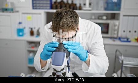 Handsome young caucasian man, a dedicated scientist, deeply engrossed in analyzing samples under the microscope at a professional medical lab. Stock Photo