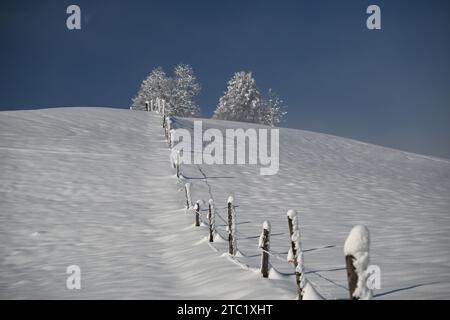 An old wooden fence is visible atop a snowy hill on a clear blue day Stock Photo