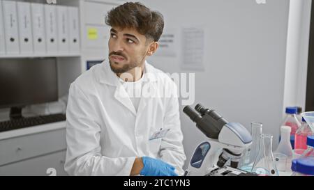 Handsome, young arabian scientist in distress, upset in laboratory over unsettling medical discovery using microscope Stock Photo