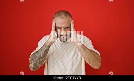 Depressed young man, alone, overwhelmed by headache and stress, expressing intense ache and sadness, standing desolate against an isolated red wall ba Stock Photo