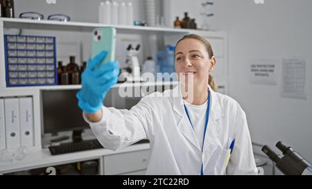 Attractive, young blonde scientist speaking on a video call, smiling while working on medical research with test tube in a laboratory Stock Photo