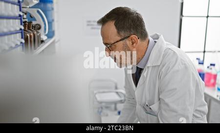 Concentrated middle-aged man with grey hair, immersed in groundbreaking science, harnesses computer power in the buzzing lab environment Stock Photo