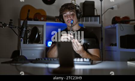 Handsome hispanic man caught in thrilling night-time gaming stream, engrossed in virtual conversation amidst the glow of his gaming room, headphones r Stock Photo