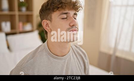 Young handsome hispanic man, deeply concentrating, resting comfortably on bed in a sunlit bedroom, practicing morning yoga, radiating calmness and bal Stock Photo