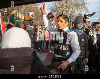 London, UK. 9 Dec 2023: A muslim man wearing a vest stating 'Stop the War' raises his hand  at a pro-Palestinian demonstration calling for an end to I Stock Photo